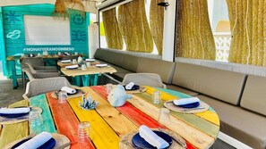 A restaurant with colorful wooden tables, white cushioned seating, and a teal wall with a hashtag sign. - Hey Peniscola (Peniscola)