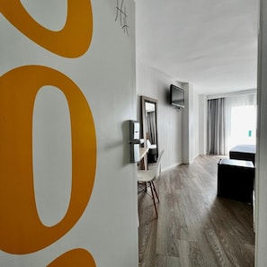 Une chambre d’hôtel moderne dotée d’une grande œuvre d’art murale, d’un téléviseur à écran plat, d’un bureau avec une chaise et d’un lit.