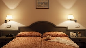 A double bed with floral bedding, two bedside lamps, a framed picture on the wall, and a nightstand with a lamp and a small plant. - Apartamentos Paya Ii (Formentera)