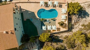 An aerial view of a hotel with a swimming pool surrounded by sun loungers and umbrellas, a terracotta roof, and a stone wall. - Apartamentos Paya Ii (Formentera)