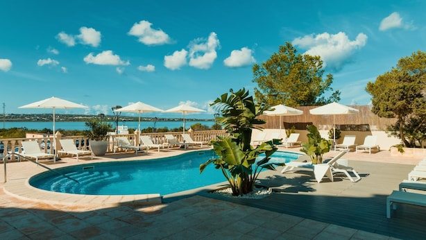 A pool area with lounge chairs, umbrellas, and a view of the sea. - Apartamentos Paya Ii (Formentera)