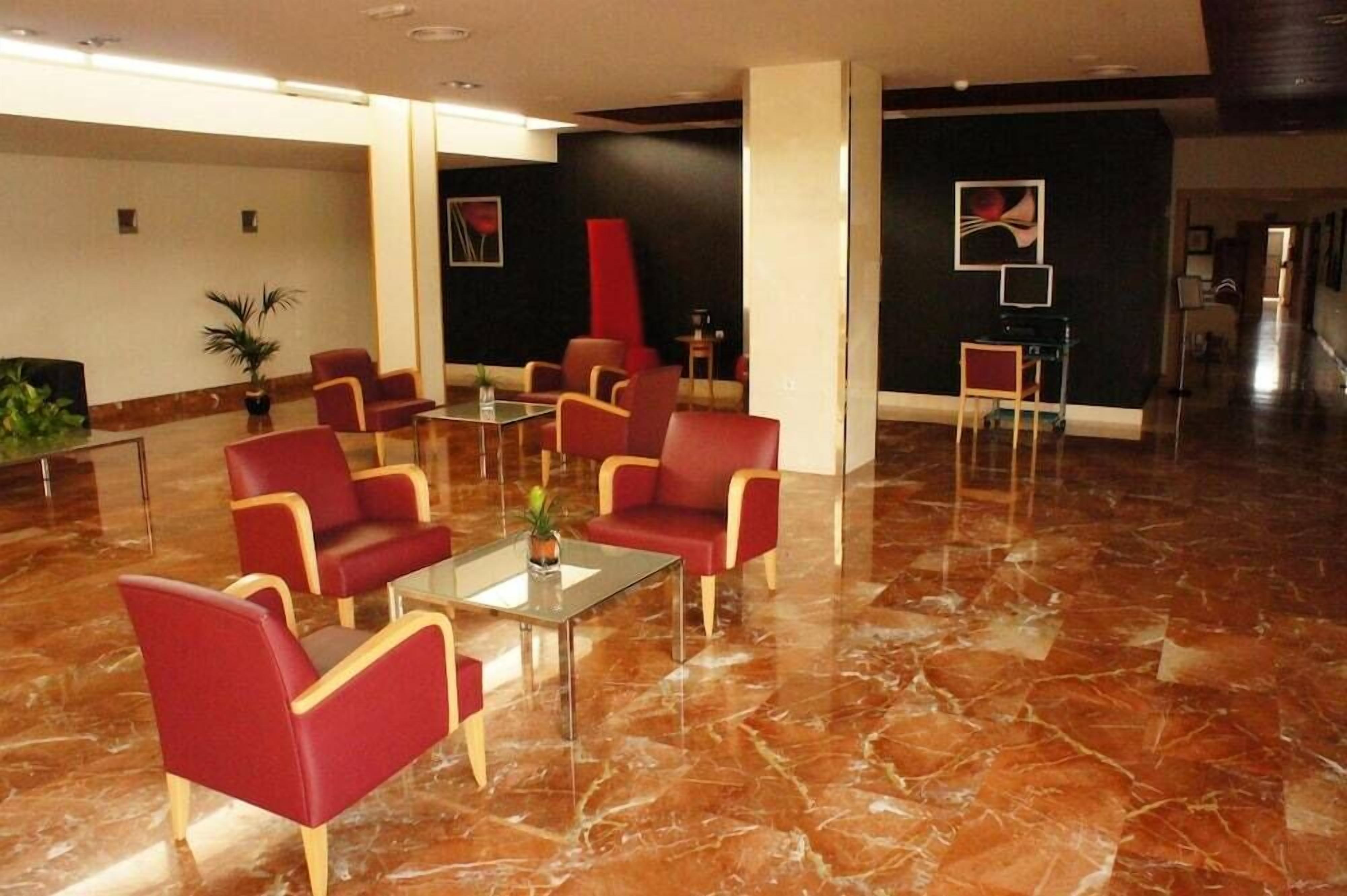 A lobby with red chairs, a glass table, and a potted plant.