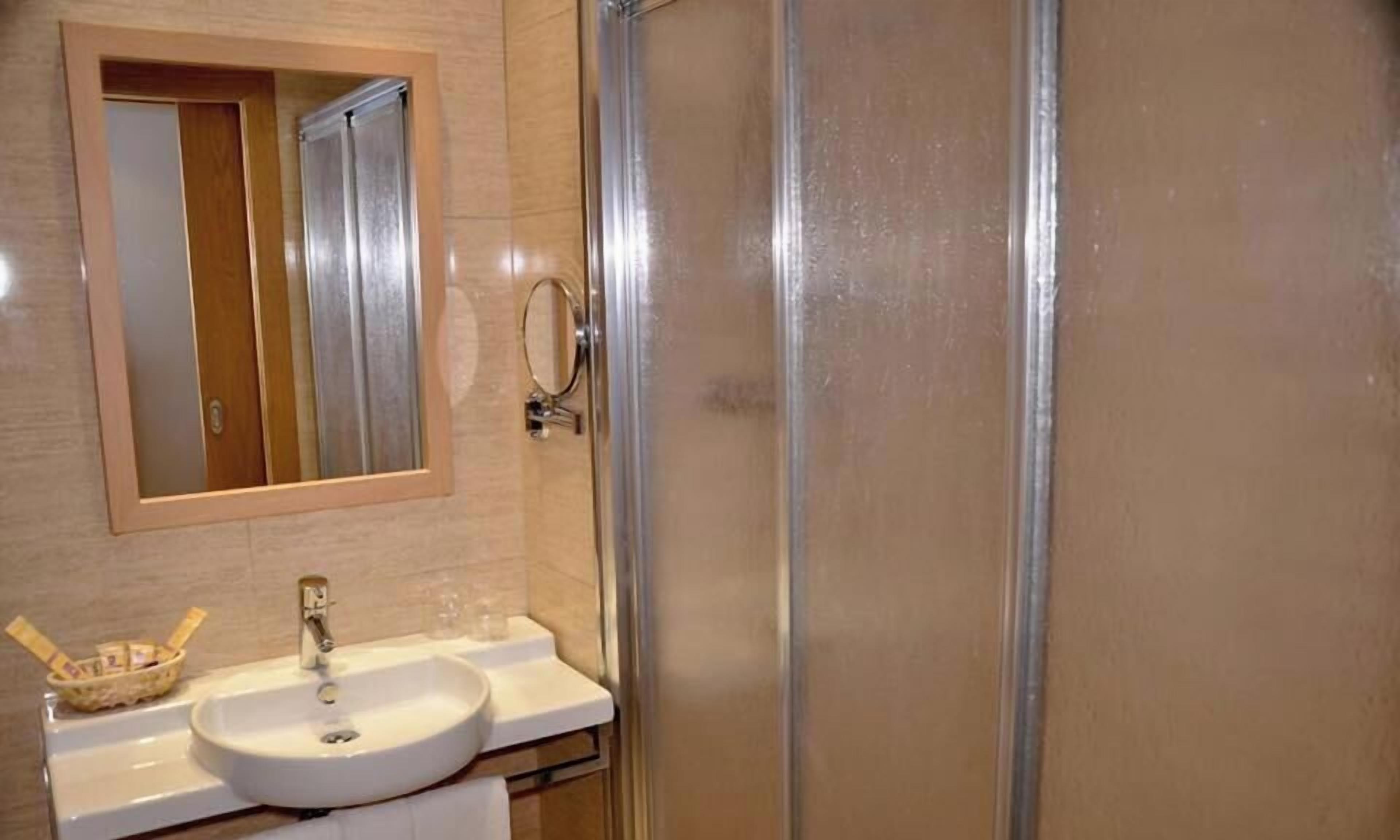 Un baño con lavamanos blanco, un espejo y cabina de ducha de vidrio.