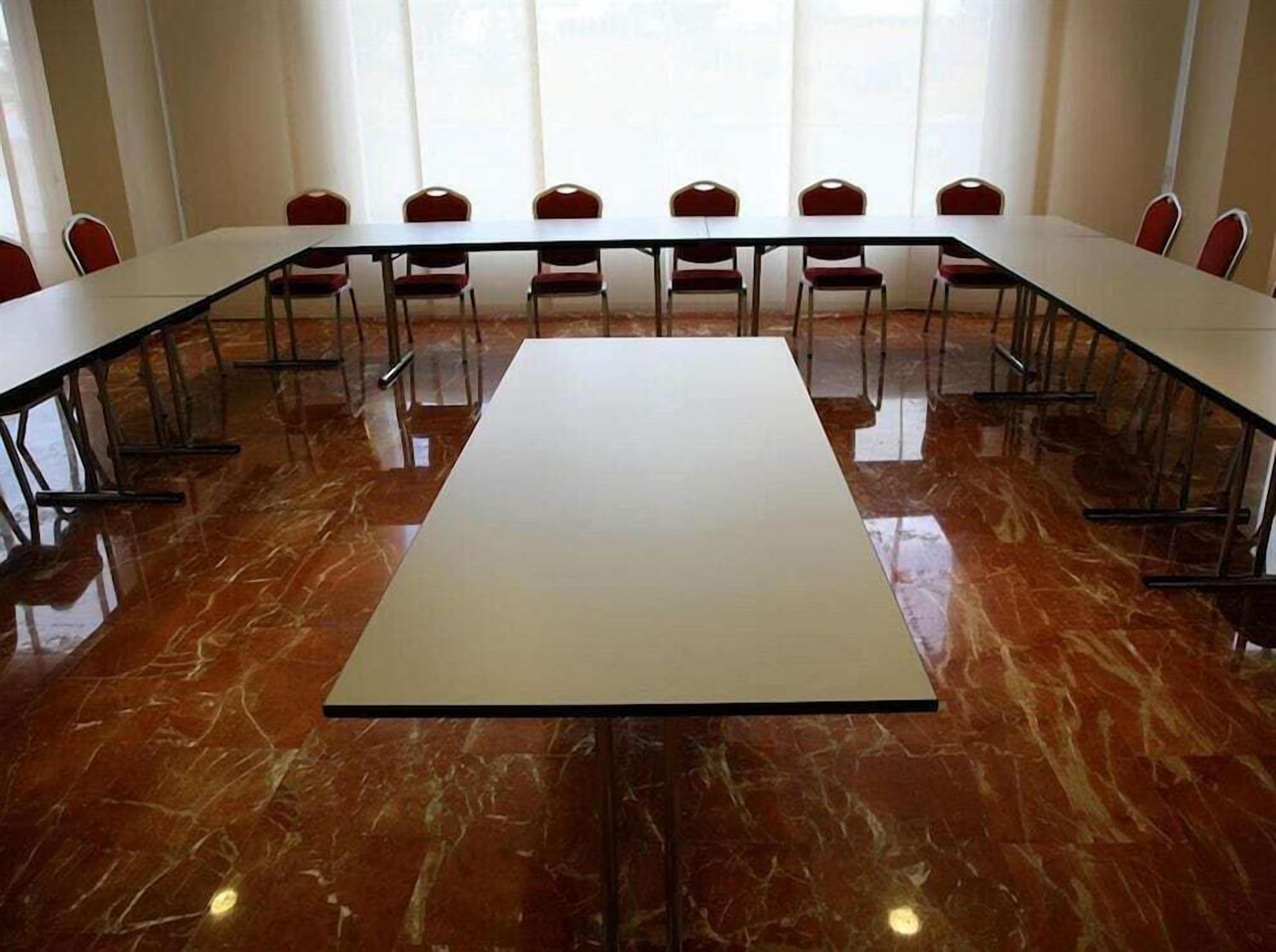 Un salón de conferencias con una larga mesa y sillas rojas, ventanas amplias y suelo de mármol.