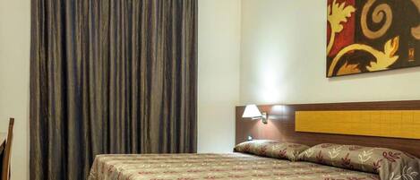 A hotel room with a bed, a nightstand, a lamp, and a large window with curtains.