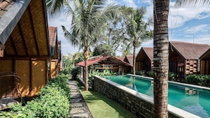 A resort with a swimming pool, palm trees, and wooden huts. - Bingin Lodge (Pecatu)
