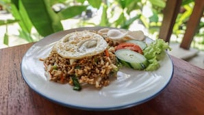 A plate of fried rice with vegetables and a fried egg on top, served on a white plate with a blue rim. - Bingin Lodge (Pecatu)