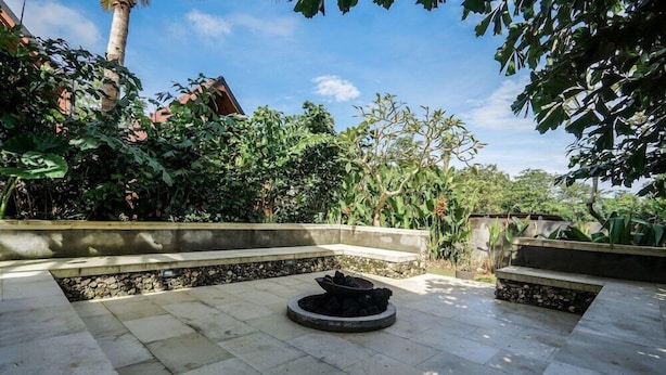 An outdoor patio area with stone flooring, a circular fire pit, and surrounding lush greenery. - Bingin Lodge (Pecatu)
