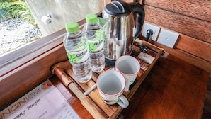 A wooden tray with water bottles, a kettle, and two mugs on a table with a menu. - Bingin Lodge (Pecatu)
