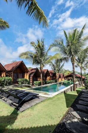 A pool area with wooden chalets, palm trees, and a clear sky. - Bingin Lodge (Pecatu)