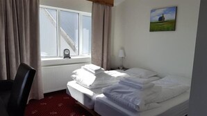Ein Hotelzimmer mit Bett, Sessel, einem Fenster mit Vorhängen, einer Lampe und einem Bild an der Wand.