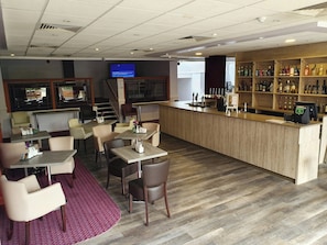 A bar area with a wooden counter, seating with tables and chairs, a television screen, and a staircase leading to an upper level. - Kegworth Hotel & Conference Centre (Derby)
