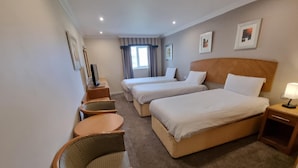 A hotel room with two single beds, a sofa, a chair, a TV, and a window with curtains. - Kegworth Hotel & Conference Centre (Derby)