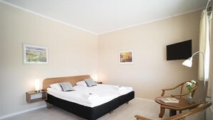 A hotel room with a large bed, bedside tables with lamps, a TV mounted on the wall, and a small table with a chair. - Sleep2night (Helsingor)