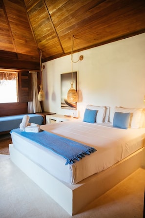 A large bed with a blue throw blanket, a bedside table with a lamp, and a window with curtains. - Hurricane Jeri (Jijoca de Jericoacoara)