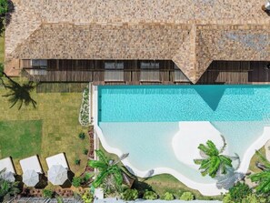 Vue aérienne d’un complexe hôtelier avec une piscine, des chaises longues et des palmiers.