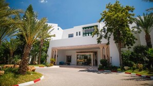 A modern building with a white facade, large glass entrance, and palm trees in the foreground. - Blumar Resort and Spa (Hammamet)