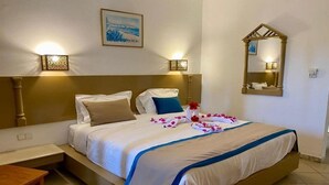 A hotel room with a large bed, two bedside lamps, a nightstand, a wooden table, and a wall-mounted mirror. - Blumar Resort and Spa (Hammamet)