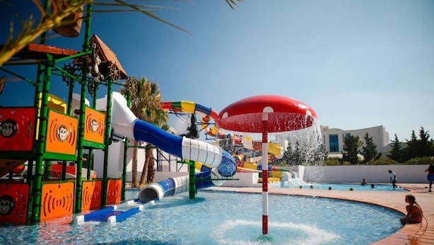 A water park with a large pool, colorful slides, and a red umbrella structure. - Blumar Resort and Spa (Hammamet)