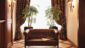 A brown leather sofa in a room with patterned curtains and two potted plants. - Hotel Schloss Pontresina Family Spa (Pontresina)