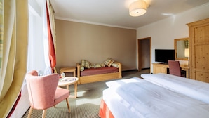 A hotel room with a bed, a sofa, a TV, a desk, and a chair. - Hotel Schloss Pontresina Family Spa (Pontresina)