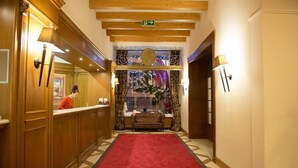A hotel lobby with a red carpet, wooden paneling, and a reception desk. - Hotel Schloss Pontresina Family Spa (Pontresina)