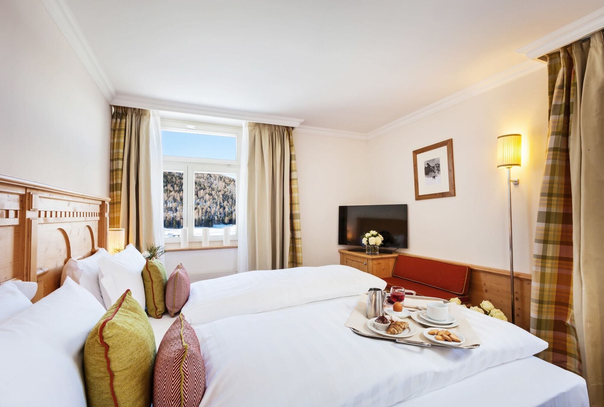Een hotelkamer met twee bedden, een televisie, een nachtkastje met lamp en een raam met gordijnen.