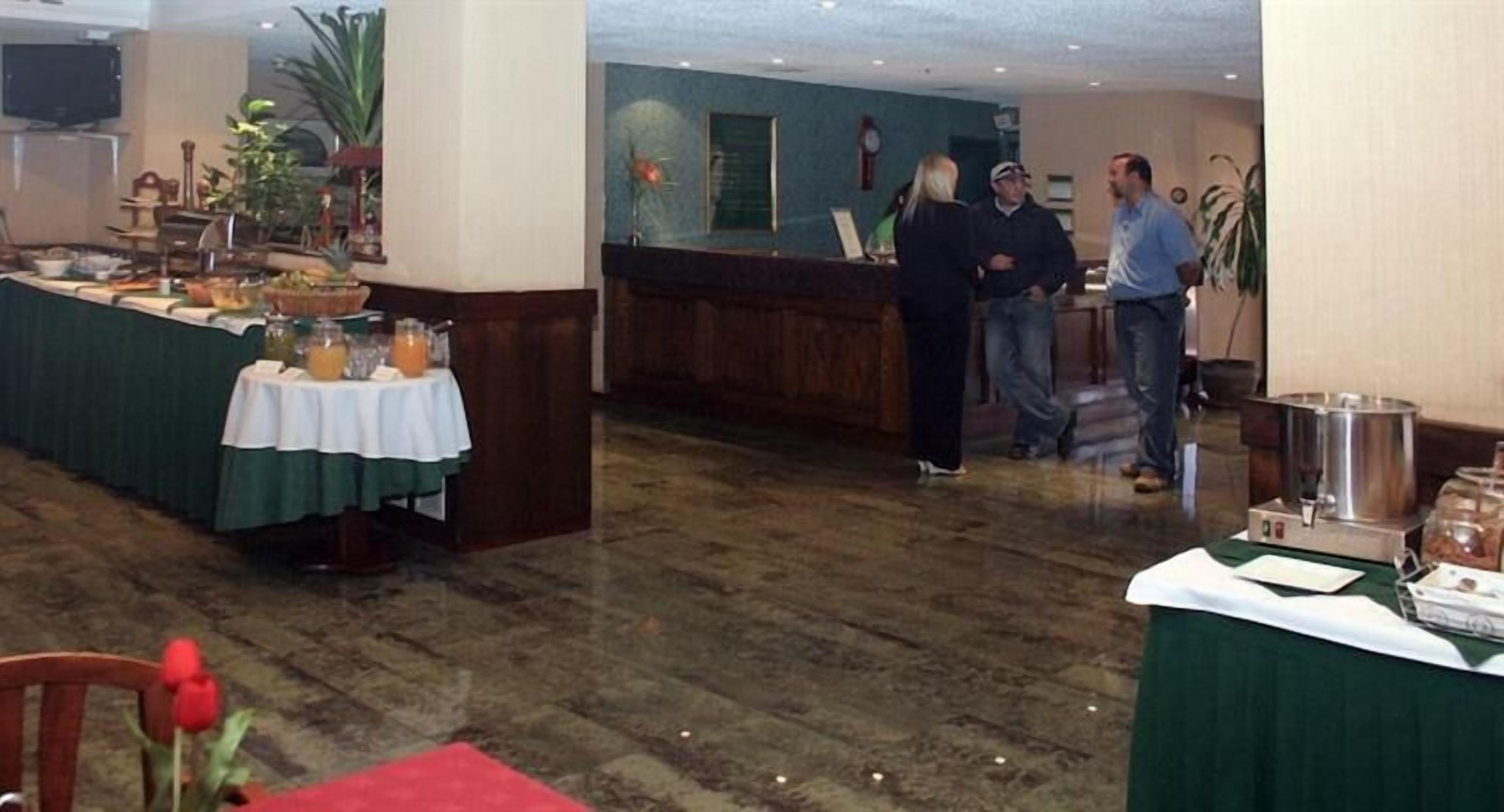 A hotel lobby with a reception desk, a buffet table with food and drinks, and a wooden floor.