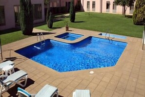 En rektangulær swimmingpool med flisebelagte omgivelser, solstole og en velholdt græsplæne.