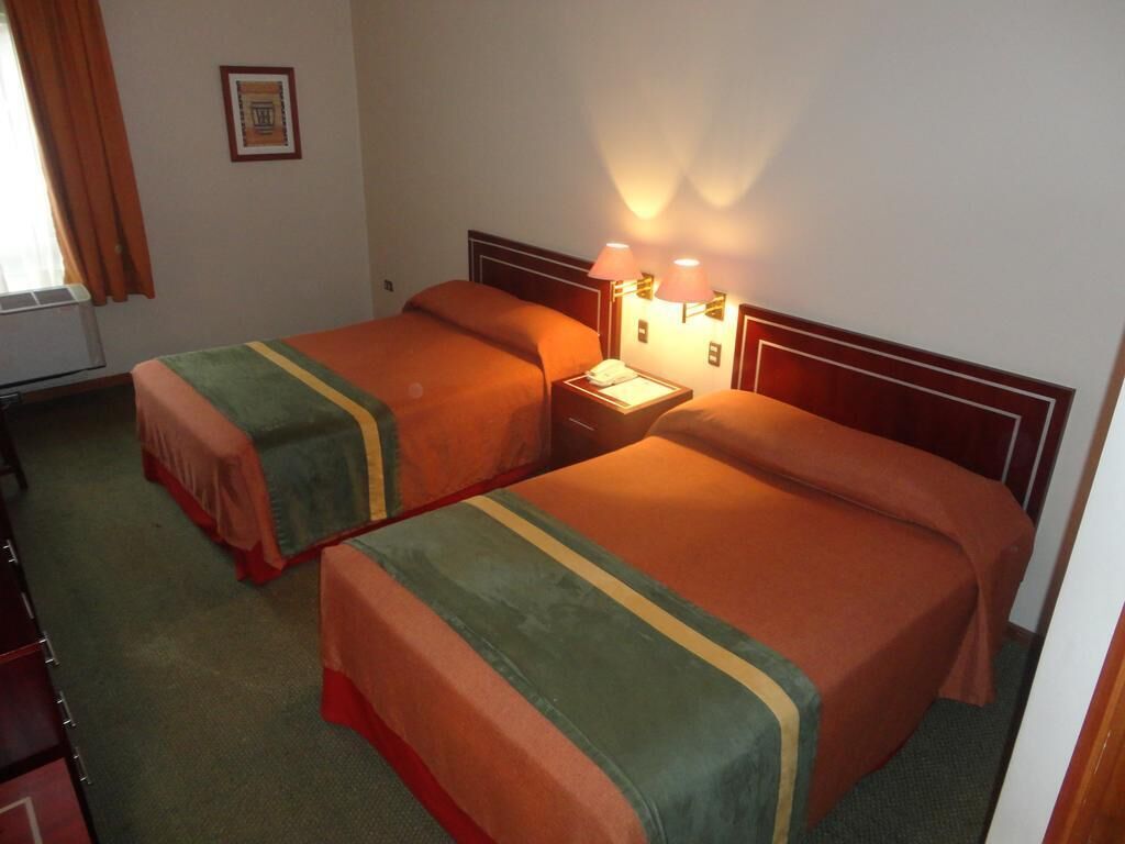 A hotel room with two beds, a nightstand with lamps, and a framed picture on the wall.