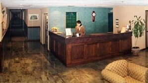 A reception area with a wooden desk, a green wall, a clock, and a potted plant. - Diego De Almagro Centro Los Angeles (Los Angeles)