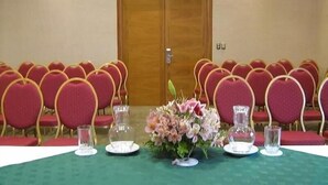 A conference room with rows of red chairs, a wooden door, and a table with water glasses and a floral centerpiece. - Diego De Almagro Centro Los Angeles (Los Angeles)