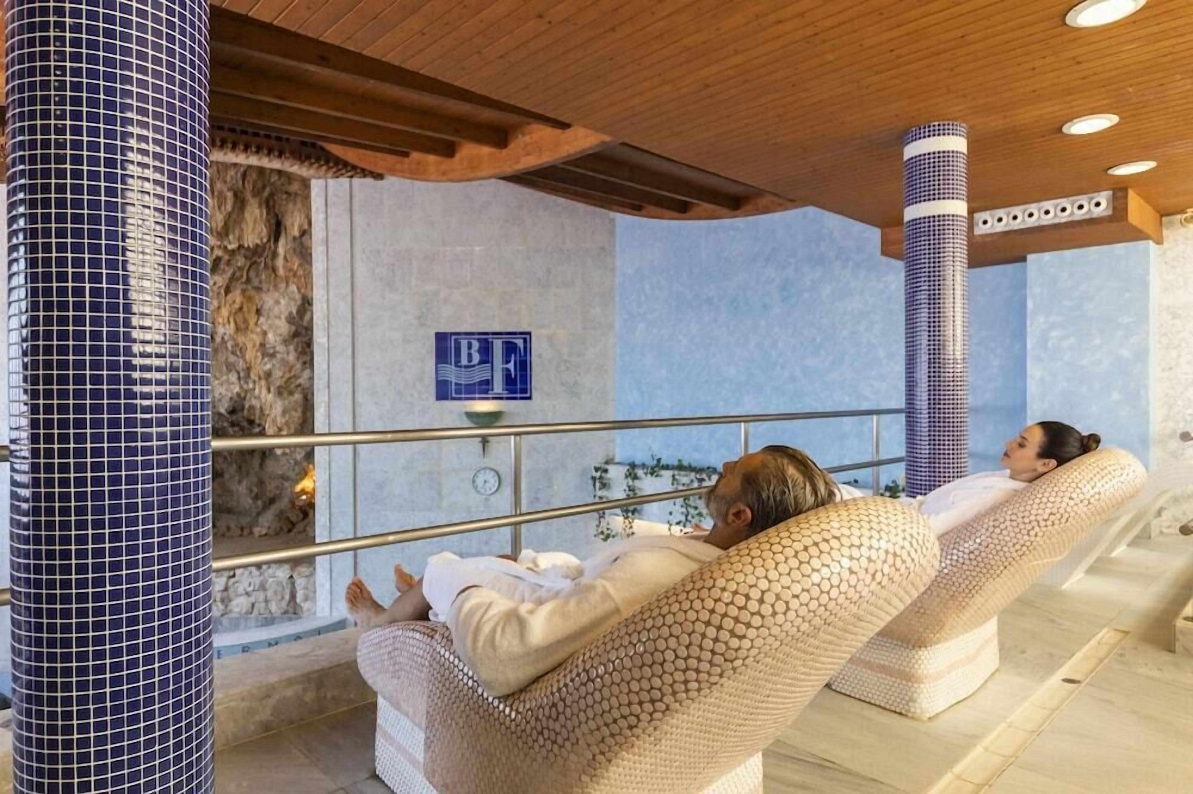 A spa area with two reclining chairs, a stone wall, and a blue-tiled column.