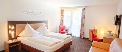 A hotel room with a double bed, a red chair, a sofa, a small table, and a TV.