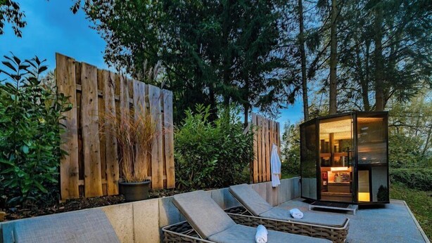 A modern outdoor lounge area with two sun loungers and a small glass structure, surrounded by wooden fences and greenery. - Waldachtal Business Balance (Waldachtal)