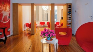 A modern interior with wooden flooring, red chairs, a central table with a flower arrangement, and a bookshelf. - Locanda di Palazzo Cicala (Genoa)