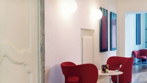 A modern interior with red chairs, a small table, and artwork on the wall. - Locanda di Palazzo Cicala (Genoa)