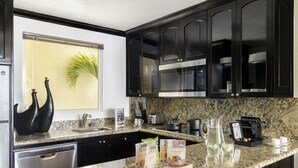 A modern kitchen with dark cabinets, granite countertops, a dishwasher, a coffee machine, and a window with a plant. - Relax in Style at Luxury Beachfront Escape at Villa Del Palmer
5-Star Oceanfront (Cancún)