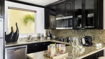 A modern kitchen with dark cabinets, granite countertops, a dishwasher, a coffee machine, and a window with a plant.
