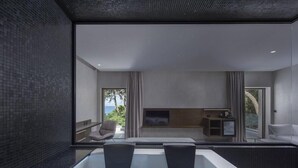 A modern interior with a large bathtub, seating area, and a view of the outdoors. - Lalibay Resort & Spa - Adults Only (Aegina)
