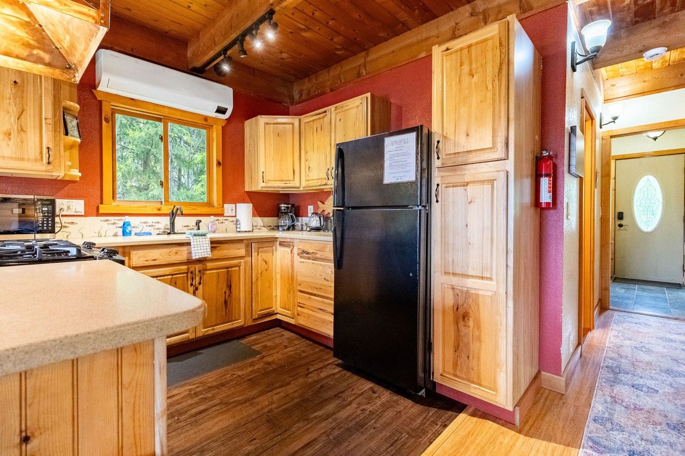 A kitchen with wooden cabinets, a black refrigerator, and a window with a view of trees.