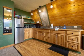 A kitchen with wooden cabinets, a stainless steel refrigerator, a microwave, and a sink with a towel. - Alaska Lakeside Cottage (Seward)
