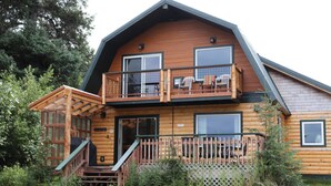 A two-story log cabin with a balcony, a staircase, and a fenced deck area. - Alaska Lakeside Cottage (Seward)