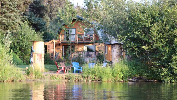 A cabin by a lake with a small dock, surrounded by dense trees. - Alaska Lakeside Cottage (Seward)