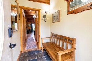 A wooden bench in a hallway with a tiled floor, a door with a keypad, and a framed picture on the wall. - Alaska Lakeside Cottage (Seward)