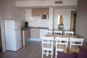 A compact kitchen with white appliances, a dining area with white chairs, and a visible microwave above the counter.