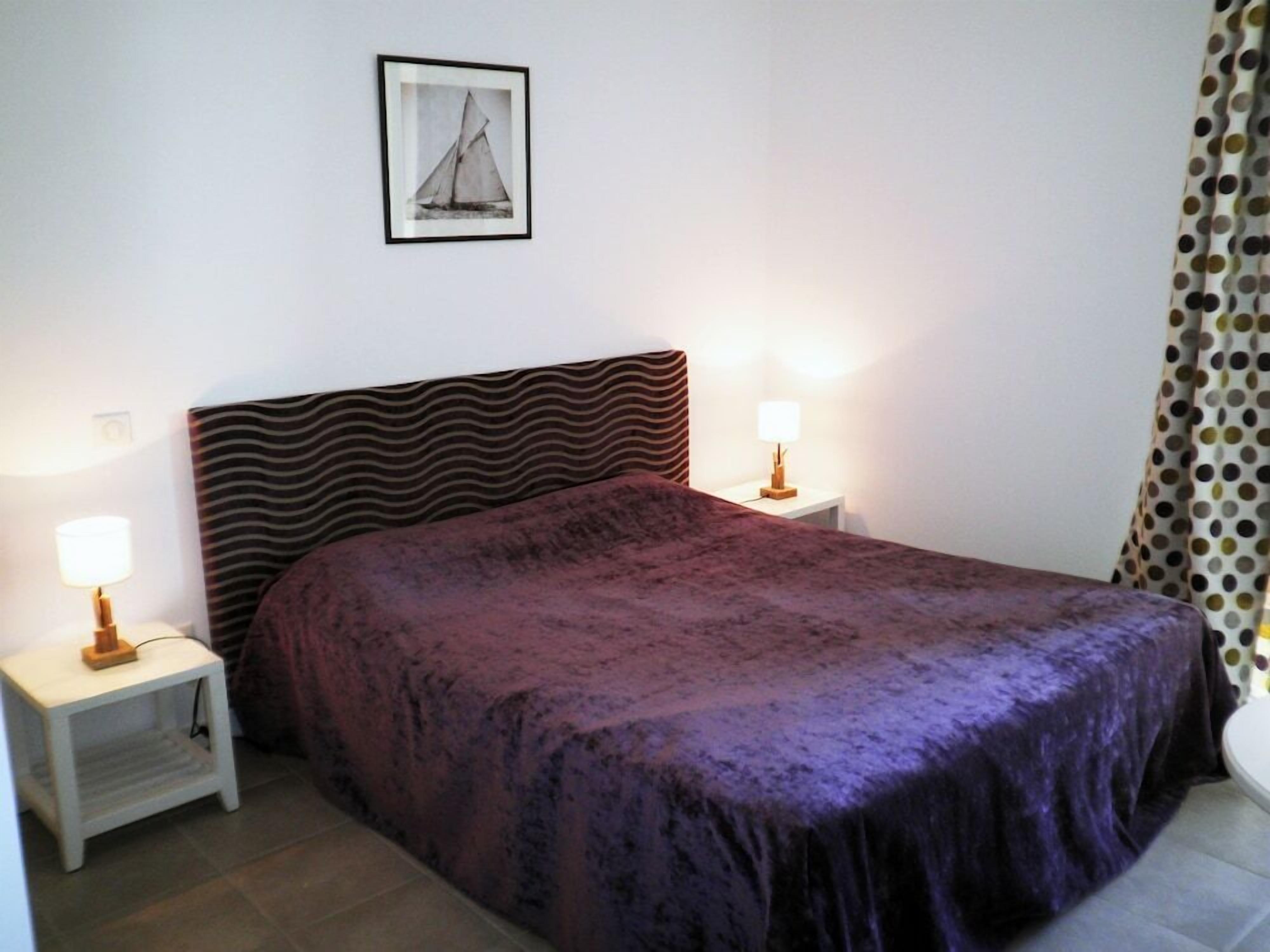 Une chambre à coucher avec un lit, deux tables de chevet avec des lampes, une tête de lit à motifs et un tableau encadré au mur.