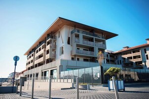 A multi-story building with balconies, a covered entrance, and a paved area in front.