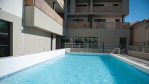 A swimming pool with a clear blue water surface, surrounded by a white tiled deck. - Résidence Nemea L'estacade (Capbreton)