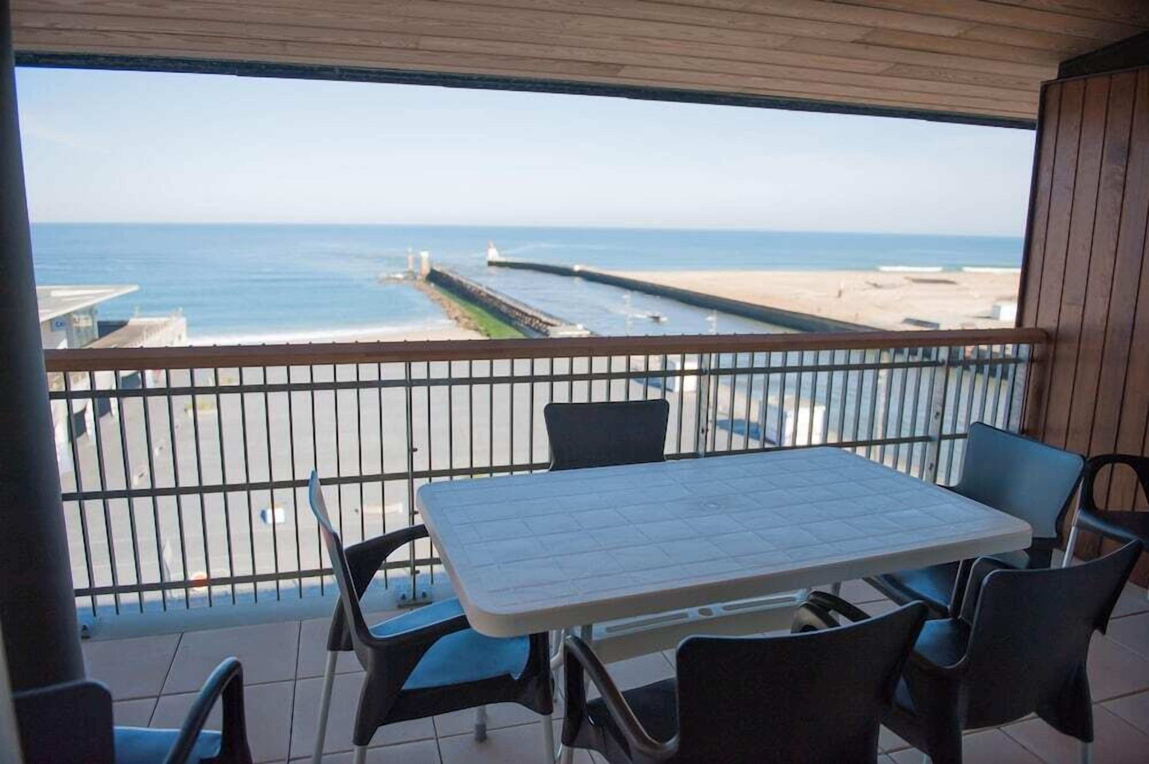 Un balcon avec une table et des chaises donnant sur une plage et une jetée.
